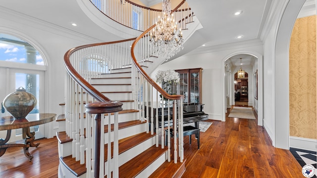 foyer entrance featuring arched walkways, a notable chandelier, wood finished floors, stairway, and crown molding