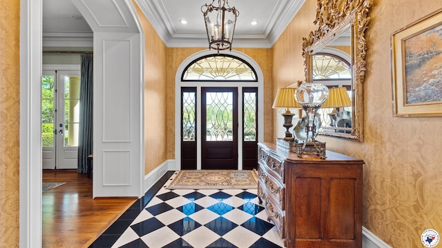 foyer entrance featuring a notable chandelier, baseboards, ornamental molding, and wallpapered walls