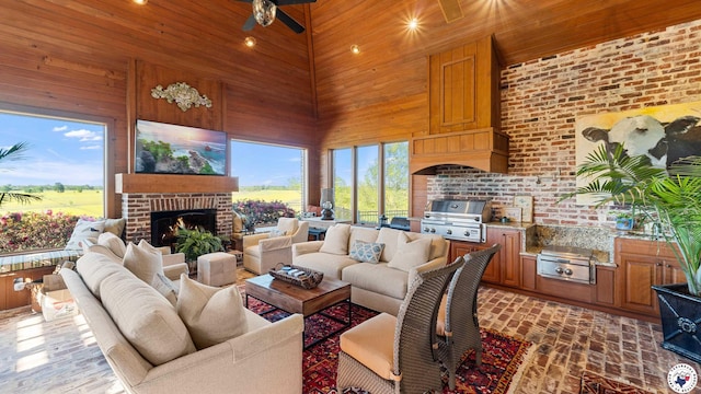 living area with wooden walls, wood ceiling, ceiling fan, a towering ceiling, and a brick fireplace