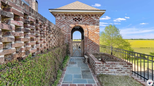 view of exterior entry with brick siding, fence, and roof with shingles