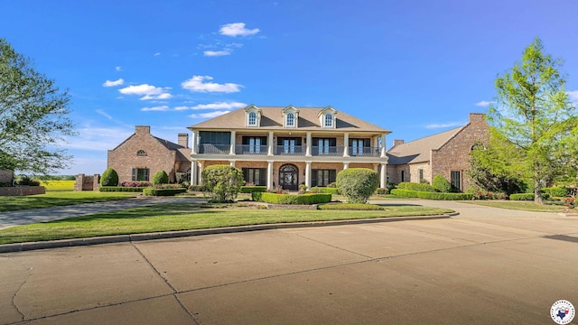 view of front of house with brick siding, covered porch, a balcony, and a front yard