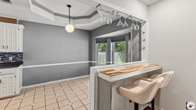 208 Jeffrey Ln, Wake Village, TX 75501 - kitchen featuring a textured ceiling, white cabinetry, a tray ceiling, a breakfast bar, and tasteful backsplash