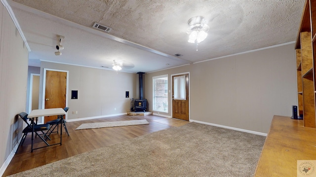 interior space featuring crown molding, a textured ceiling, a wood stove, carpet, and ceiling fan