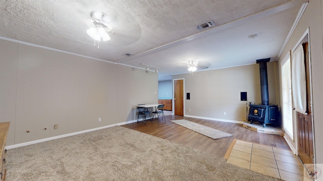 interior space with crown molding, ceiling fan, a textured ceiling, and a wood stove