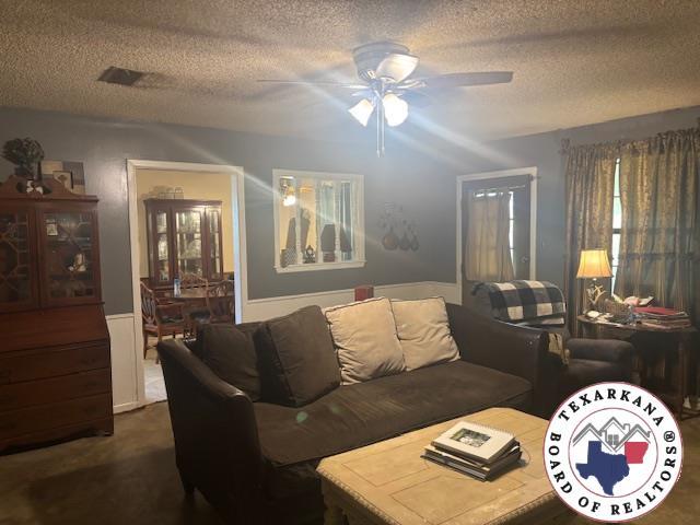 4903 Charleston St, Texarkana, AR 71854 - living area with a textured ceiling, a ceiling fan, dark colored carpet, and a wainscoted wall