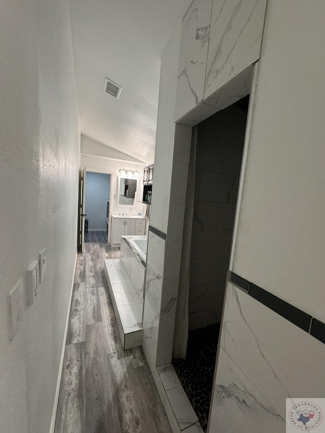 corridor with hardwood / wood-style flooring and vaulted ceiling