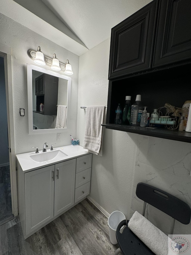 bathroom featuring baseboards, wood finished floors, lofted ceiling, a textured wall, and vanity