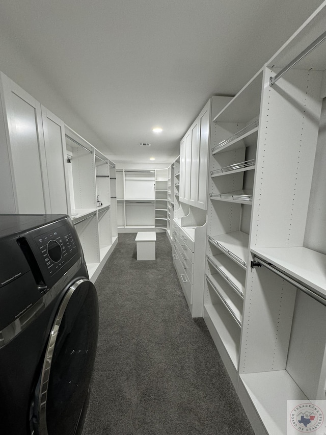 spacious closet featuring washer / dryer and dark colored carpet