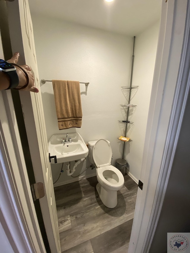 half bathroom featuring a sink, toilet, baseboards, and wood finished floors