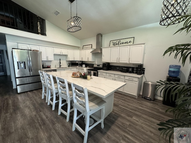 kitchen with appliances with stainless steel finishes, white cabinetry, decorative light fixtures, light stone counters, and wall chimney exhaust hood