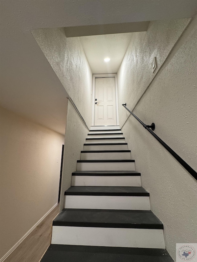 stairs with a textured wall, baseboards, and wood finished floors