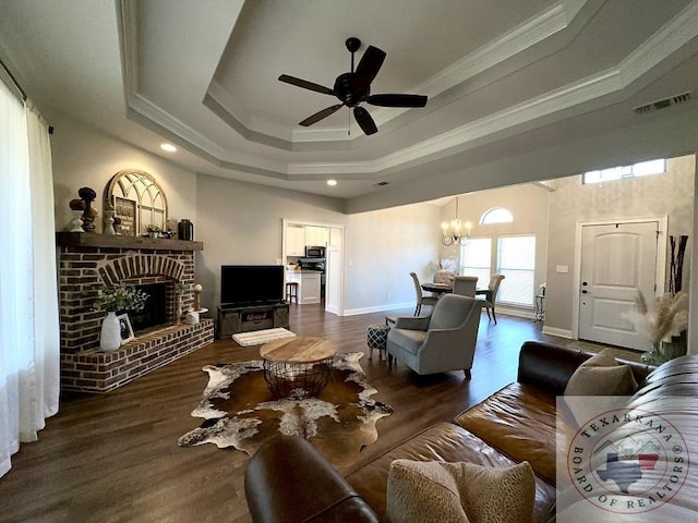 living room featuring ceiling fan with notable chandelier, dark hardwood / wood-style floors, a fireplace, and a tray ceiling