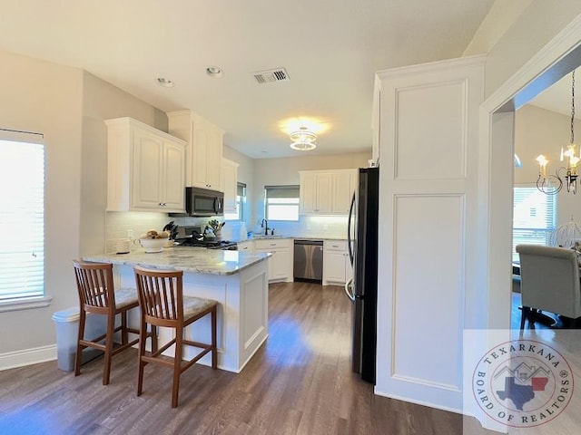 kitchen with kitchen peninsula, dark wood-type flooring, white cabinetry, a chandelier, and stainless steel appliances