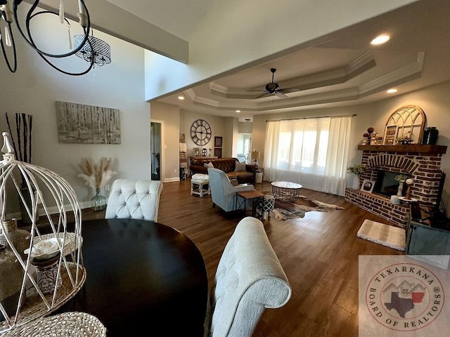 dining space with a brick fireplace, dark hardwood / wood-style flooring, a raised ceiling, and ceiling fan