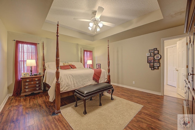 bedroom with ceiling fan, a textured ceiling, dark hardwood / wood-style flooring, and a raised ceiling