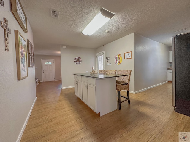 kitchen with light wood-type flooring, white cabinetry, a textured ceiling, a center island, and a breakfast bar