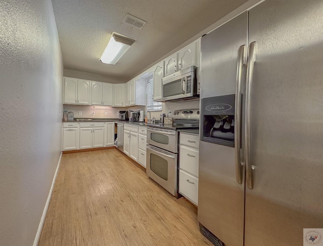 kitchen featuring appliances with stainless steel finishes, sink, light wood-type flooring, white cabinetry, and a textured ceiling