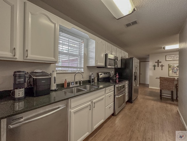 kitchen with sink, white cabinets, a textured ceiling, light hardwood / wood-style floors, and stainless steel appliances