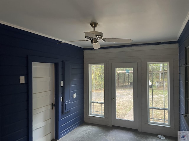 doorway featuring concrete floors, crown molding, wood walls, and ceiling fan