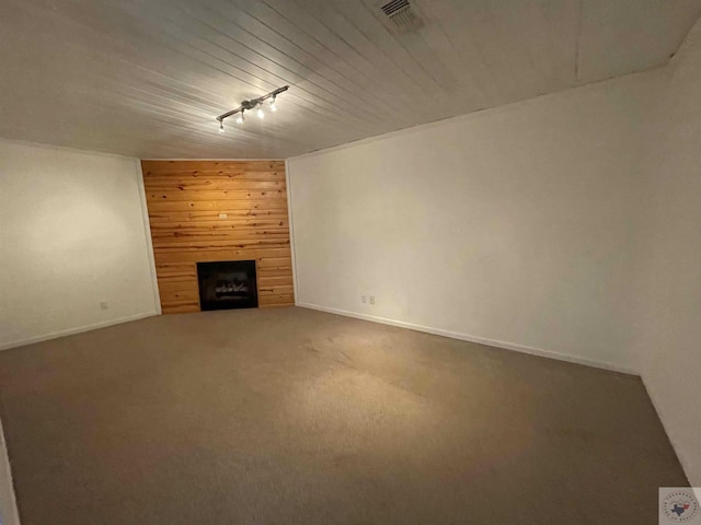 unfurnished living room with track lighting, carpet flooring, wooden walls, and a tiled fireplace