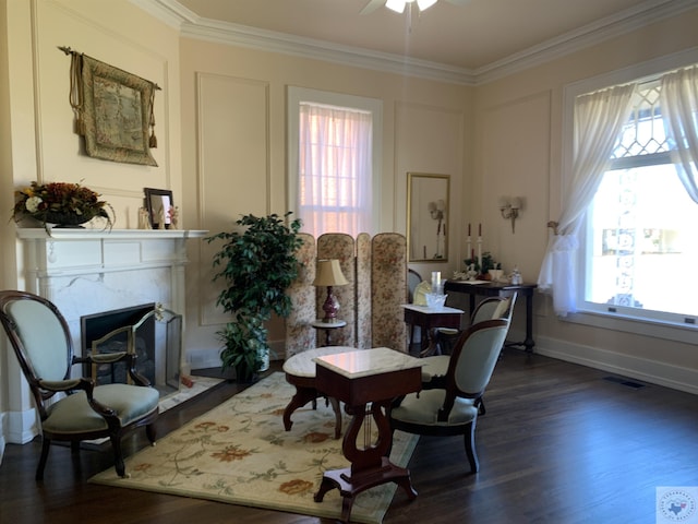 sitting room with ornamental molding, a premium fireplace, wood finished floors, and a wealth of natural light