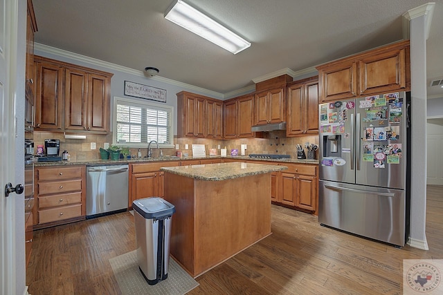 kitchen featuring sink, light stone counters, a center island, stainless steel appliances, and hardwood / wood-style floors