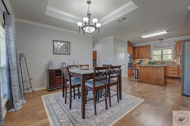 dining space featuring sink, crown molding, light wood-type flooring, a tray ceiling, and a notable chandelier