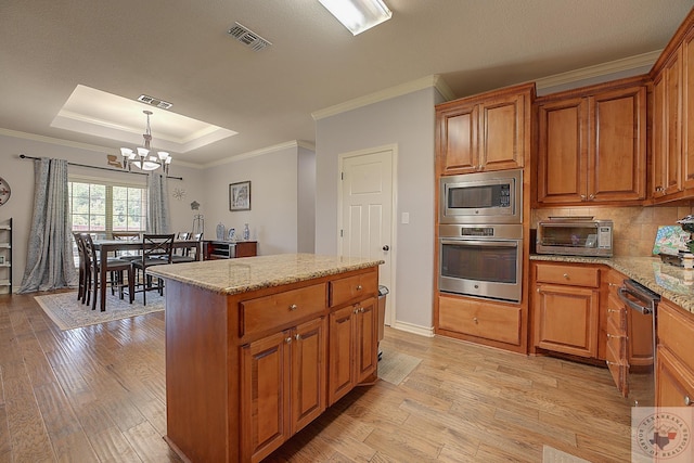 kitchen with pendant lighting, appliances with stainless steel finishes, a kitchen island, a raised ceiling, and light stone counters