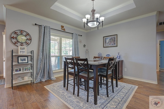 dining room featuring a raised ceiling, dark hardwood / wood-style flooring, crown molding, and a chandelier