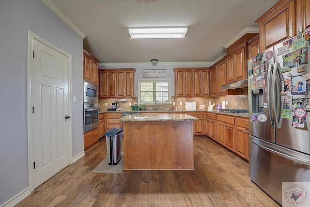 kitchen with light hardwood / wood-style flooring, appliances with stainless steel finishes, light stone counters, ornamental molding, and a kitchen island