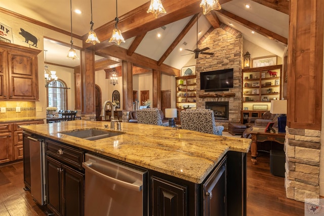 kitchen featuring beamed ceiling, a stone fireplace, hanging light fixtures, sink, and an island with sink