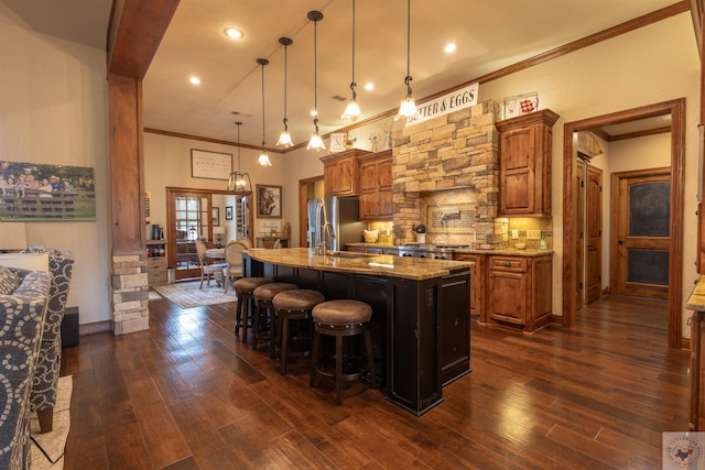 kitchen featuring hanging light fixtures, sink, dark wood-type flooring, light stone counters, and a center island with sink