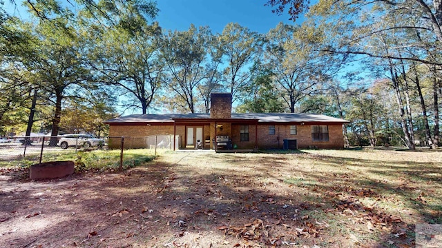 back of property with brick siding, french doors, a chimney, and fence