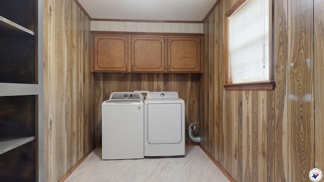 clothes washing area featuring marble finish floor, washer and clothes dryer, wooden walls, and cabinet space