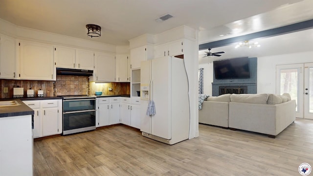 kitchen with under cabinet range hood, white refrigerator with ice dispenser, dark countertops, light wood finished floors, and range with two ovens