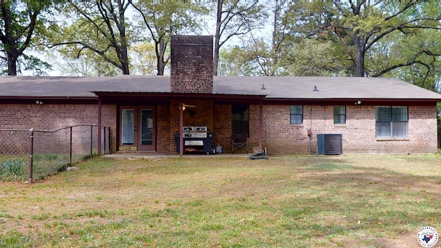 back of property featuring a chimney, fence, brick siding, a lawn, and central AC