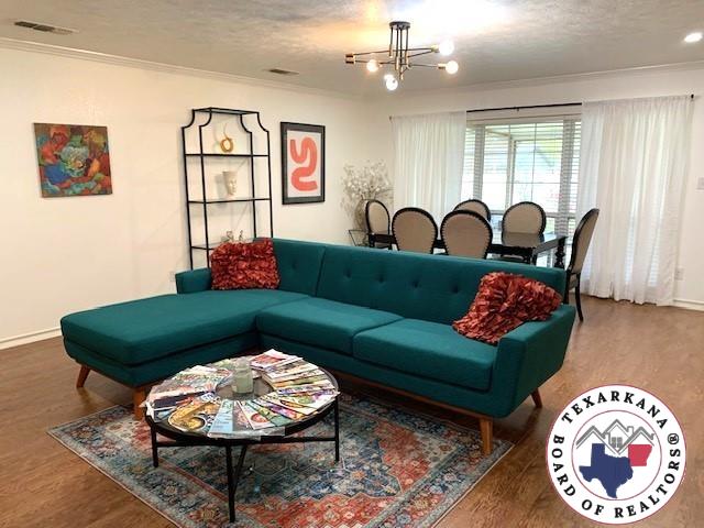 living room with baseboards, ornamental molding, wood finished floors, and a notable chandelier
