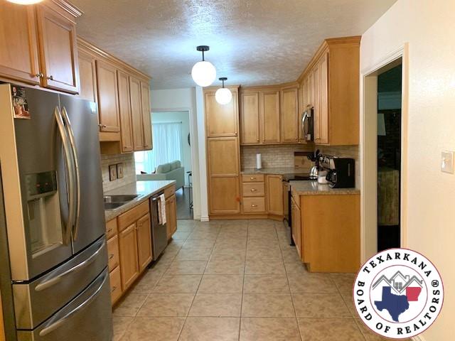 kitchen with decorative backsplash, light tile patterned flooring, hanging light fixtures, and stainless steel appliances
