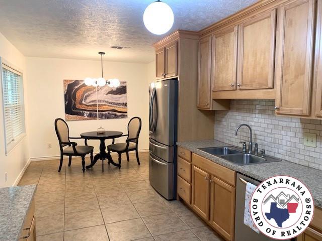 kitchen with backsplash, a textured ceiling, a sink, freestanding refrigerator, and an inviting chandelier