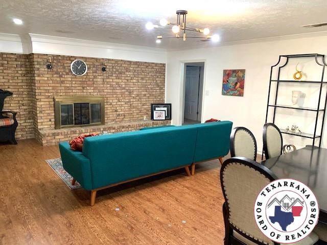 living room with a textured ceiling, visible vents, wood finished floors, an inviting chandelier, and ornamental molding