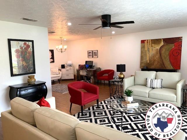 living room with a textured ceiling, ceiling fan with notable chandelier, wood finished floors, and visible vents