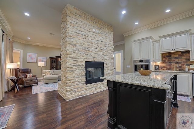 kitchen with light stone countertops, a kitchen island, white cabinetry, dark hardwood / wood-style floors, and stainless steel oven