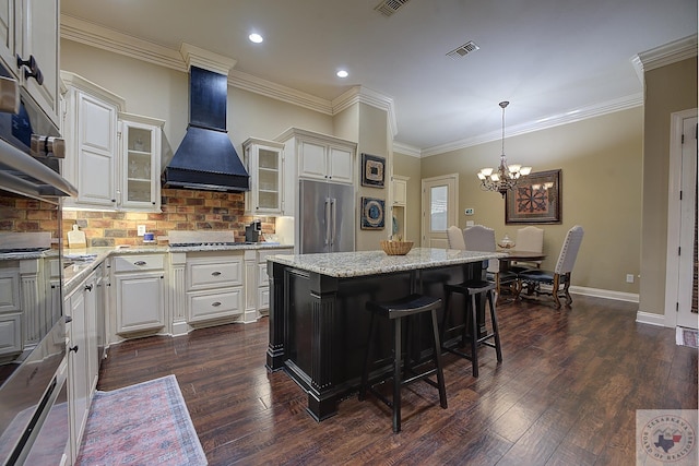 kitchen with hanging light fixtures, appliances with stainless steel finishes, custom exhaust hood, a kitchen island, and decorative backsplash