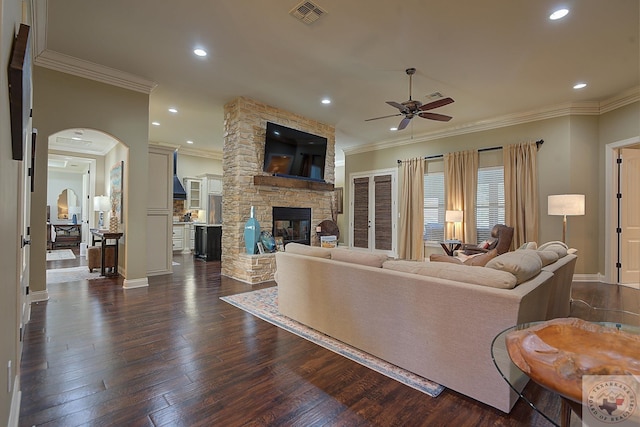 living room featuring ceiling fan, a stone fireplace, ornamental molding, and dark hardwood / wood-style floors