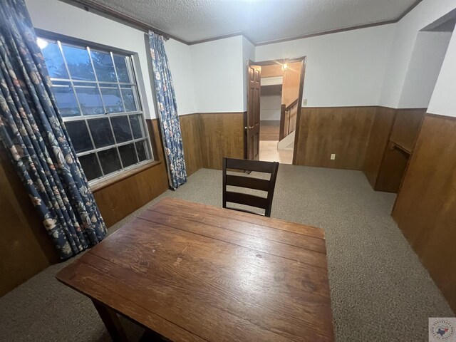 dining space featuring wood walls, crown molding, a textured ceiling, and light colored carpet