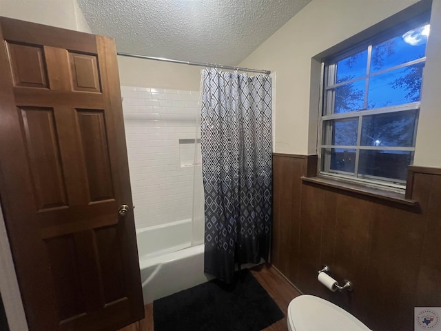 bathroom with a textured ceiling, hardwood / wood-style floors, shower / bath combination with curtain, toilet, and wood walls