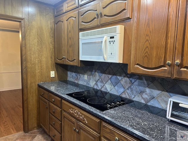 kitchen with backsplash, dark stone countertops, dark tile patterned flooring, and black electric cooktop