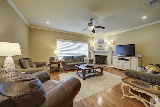 living room with light wood-type flooring, ceiling fan, ornamental molding, and a textured ceiling