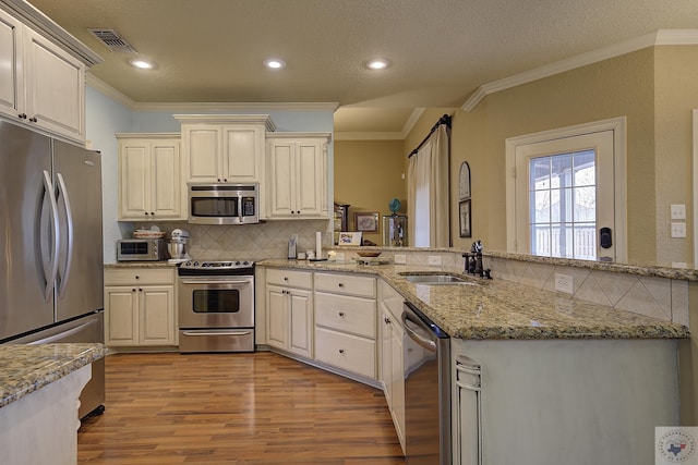 kitchen featuring kitchen peninsula, appliances with stainless steel finishes, sink, light stone counters, and light hardwood / wood-style floors