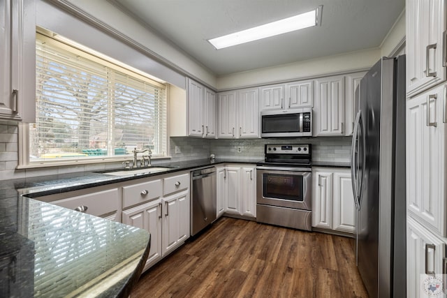 kitchen with dark countertops, appliances with stainless steel finishes, dark wood finished floors, and a sink